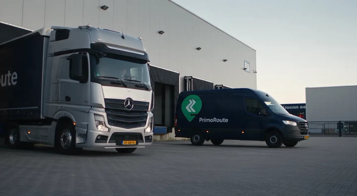 A PrimoRoute-branded delivery van and a truck parked outside a distribution centre.
